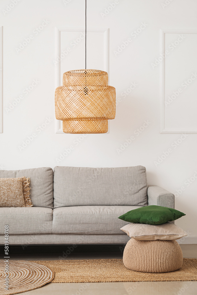 Interior of light living room with grey couch, pouf and pillows