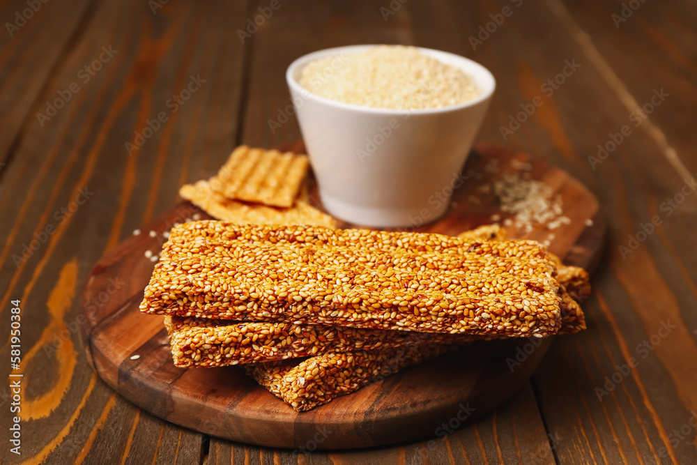 Board with tasty kozinaki and sesame seeds on wooden background