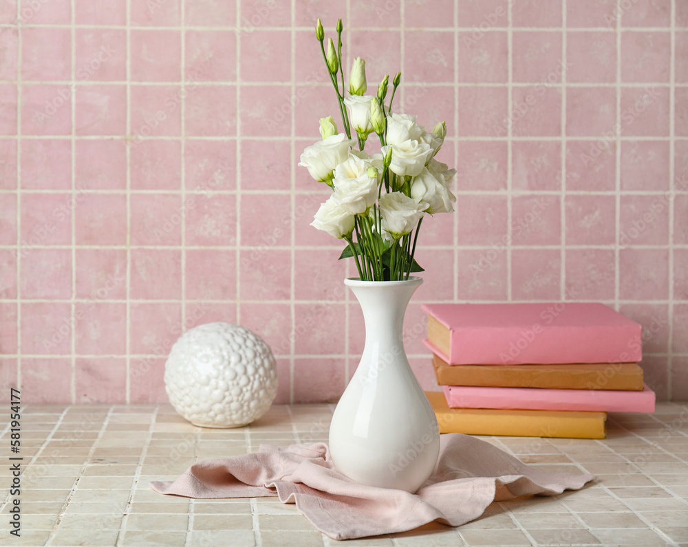 Vase with beautiful eustoma flowers, books and decor on color tile background