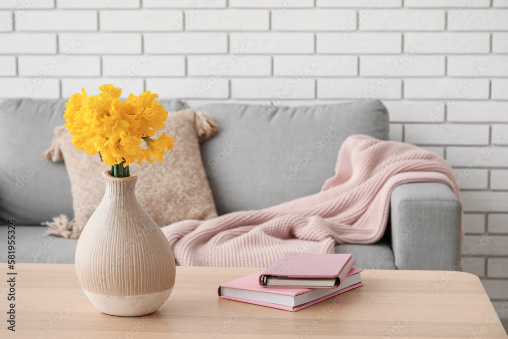 Vase with narcissus flowers and books on table in living room