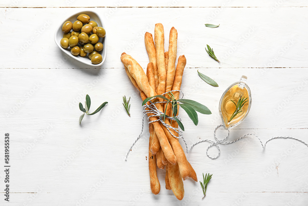 Bunch of tasty Italian Grissini and bowl with green olives on light wooden background