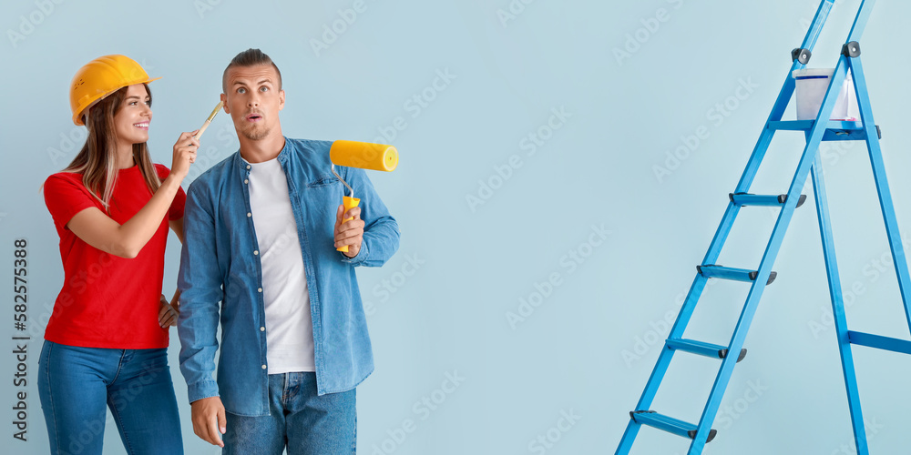 Happy young couple with paint roller, brush and ladder making repair in their new house