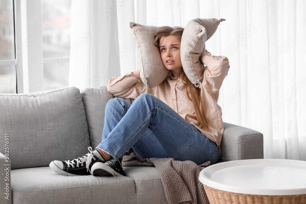 Upset young woman with pillows suffering from loud noise at home