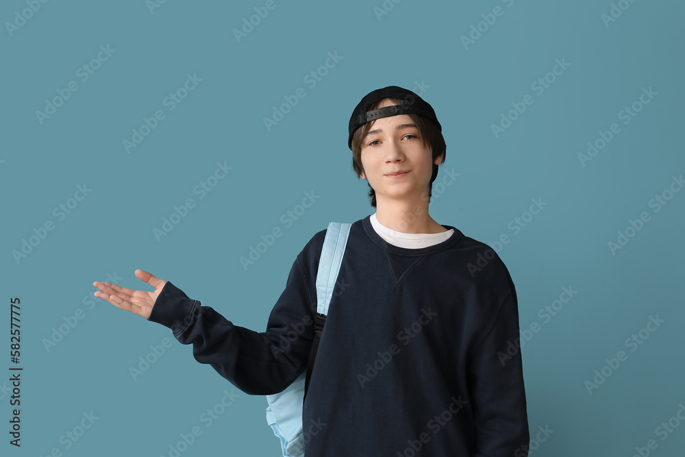 Male student with backpack showing something on blue background