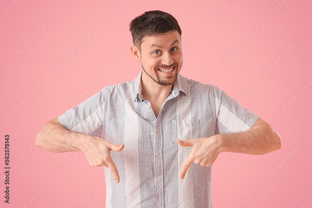 Handsome man in shirt pointing at something on pink background