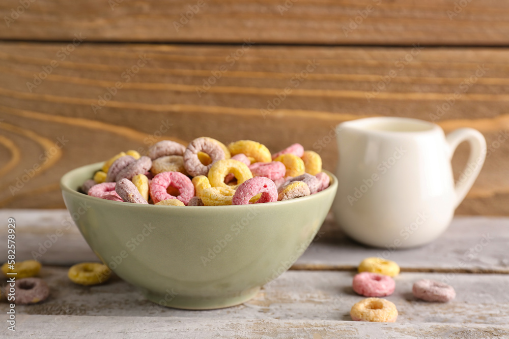 Bowl of colorful cereal rings and pitcher with milk on grey wooden table