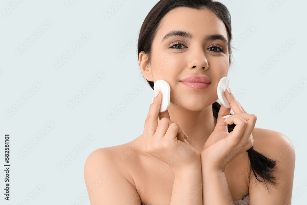 Young woman removing makeup with cotton pads on light background