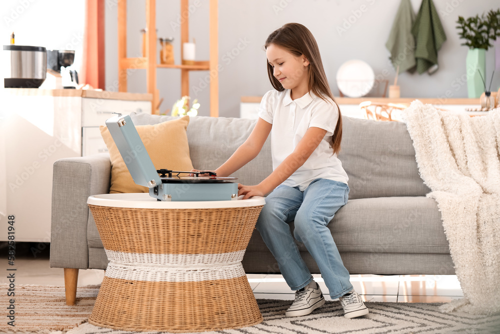 Little girl with record player sitting on sofa at home