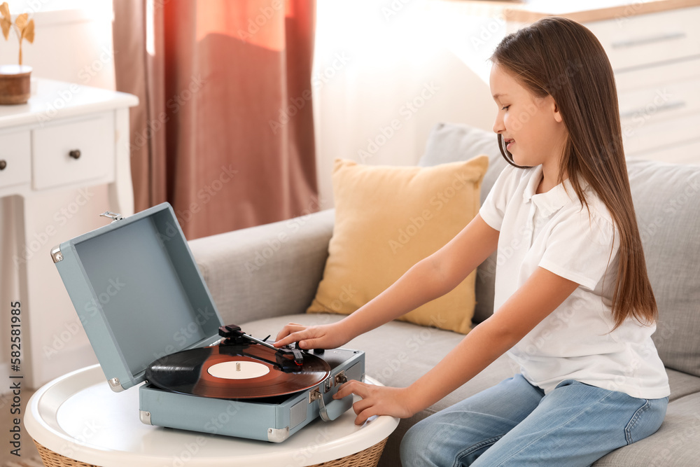 Little girl with record player sitting on sofa at home