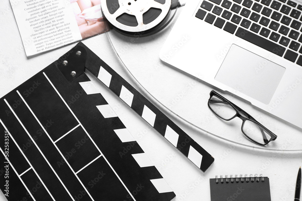 Movie clapper with film reel, eyeglasses and laptop on white background