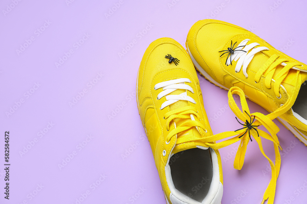 Sneakers with tied shoe laces and spiders on lilac background. April Fools Day celebration