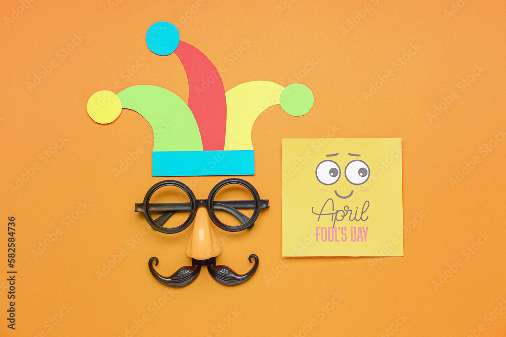 Paper with text APRIL FOOLS DAY, paper hat and disguise on color background