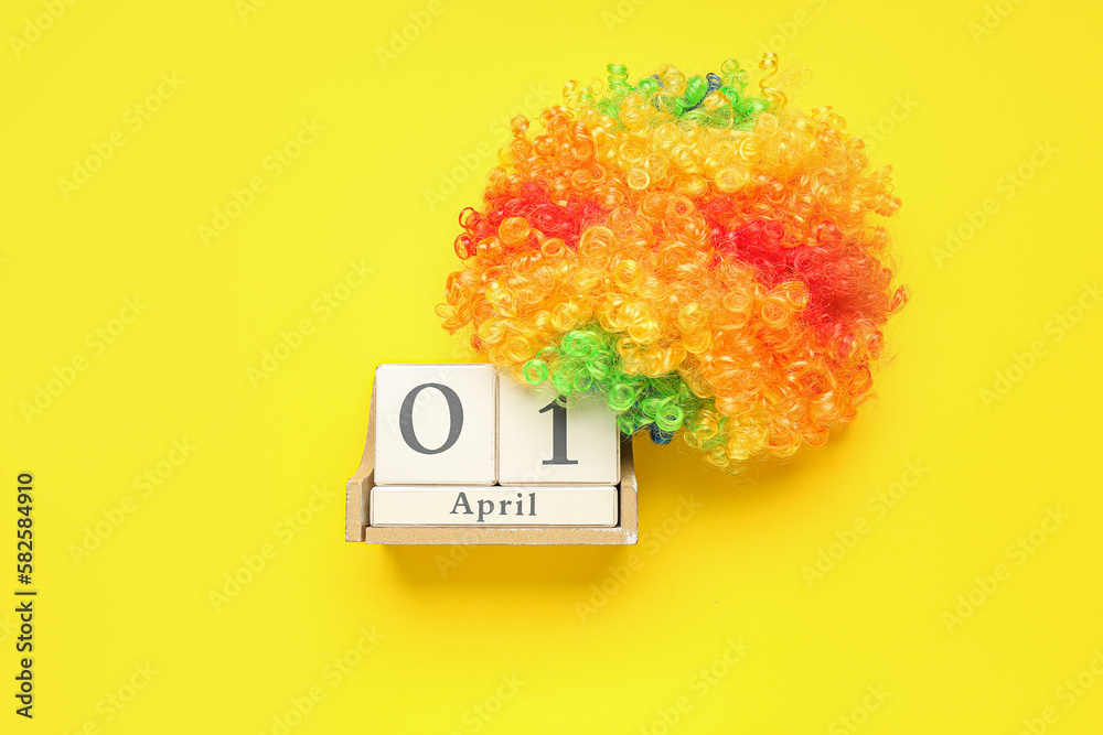 Calendar with date of April Fools Day and clown wig on yellow background