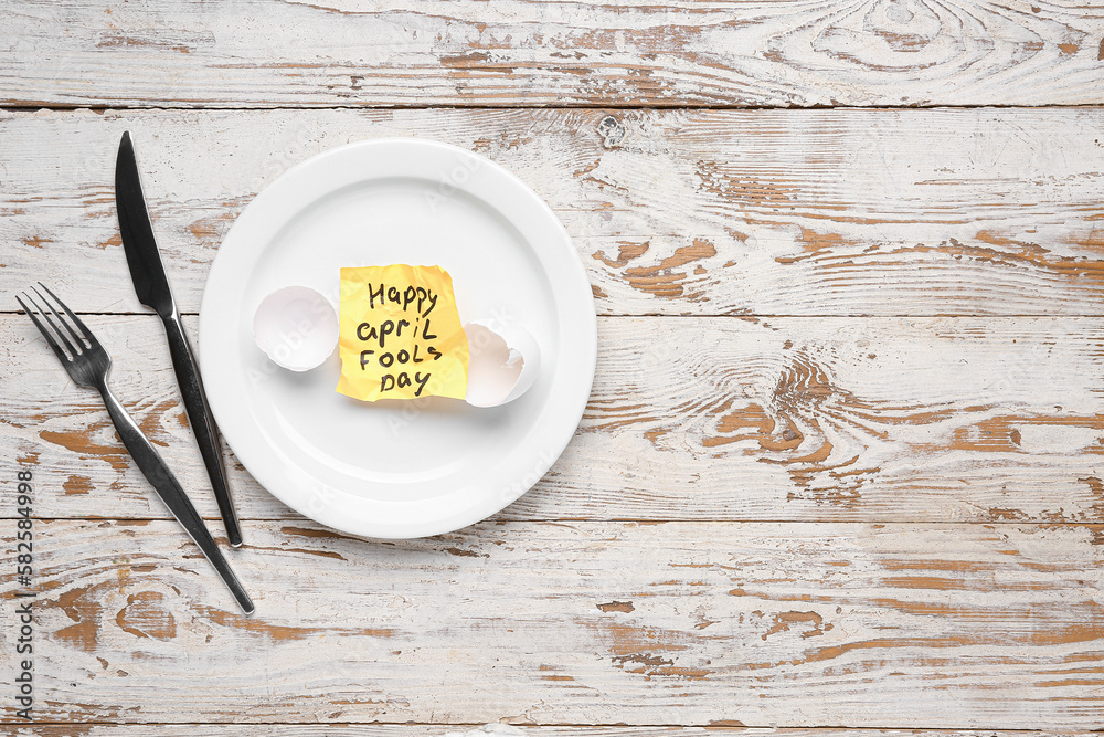 Paper with text HAPPY APRIL FOOLS DAY and table setting on white wooden background