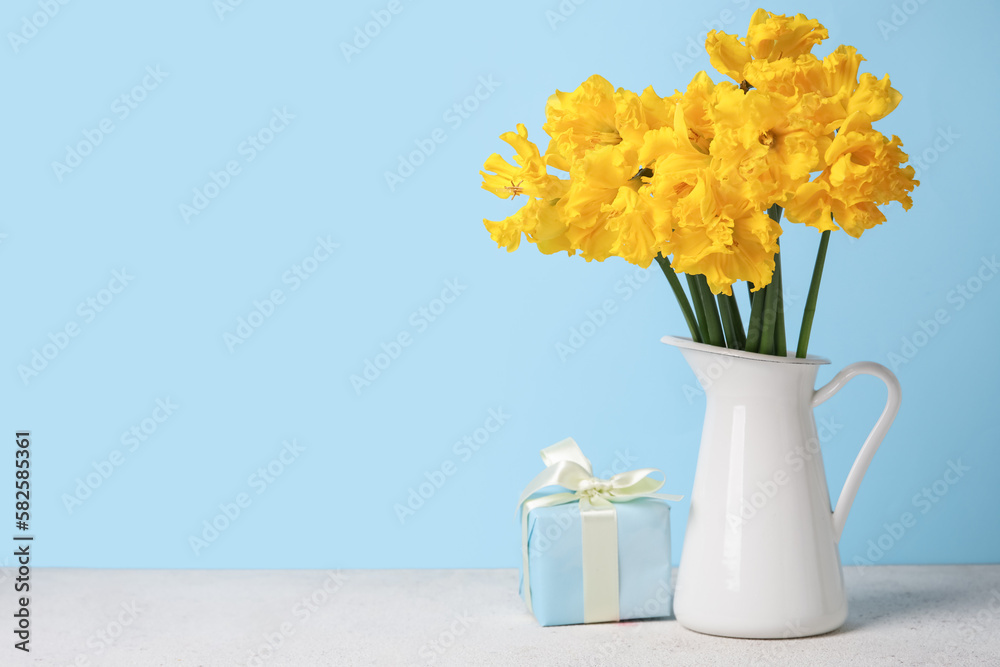 Vase with narcissus flowers and gift on table near blue wall