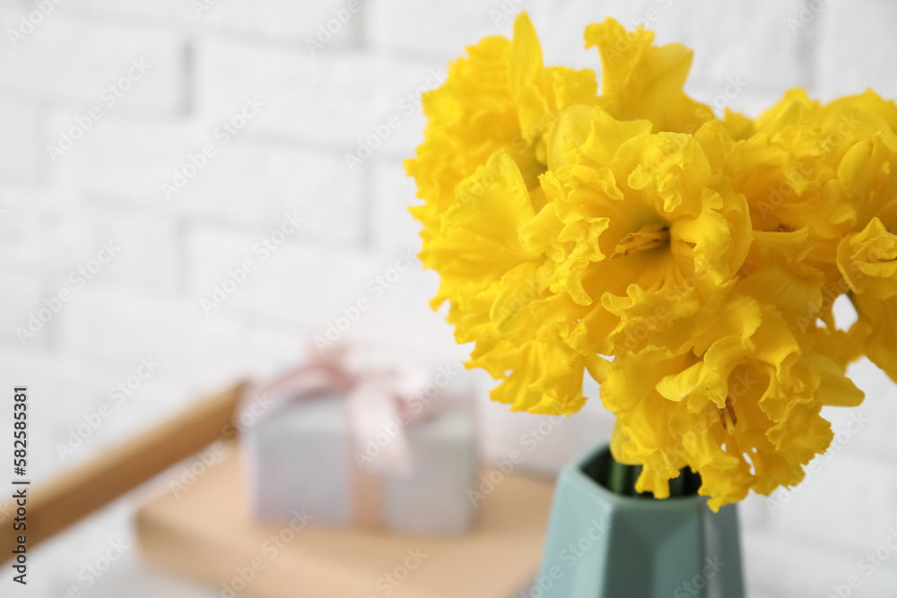 Vase with yellow narcissus flowers in room, closeup