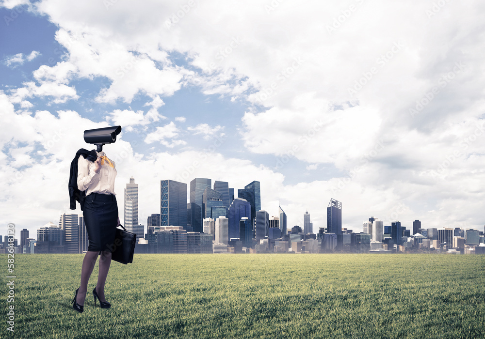 Camera headed woman standing on green grass against modern cityscape