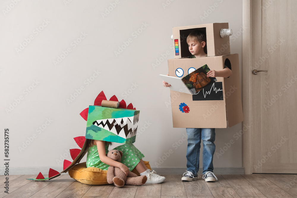 Little children in cardboard costumes playing near light wall