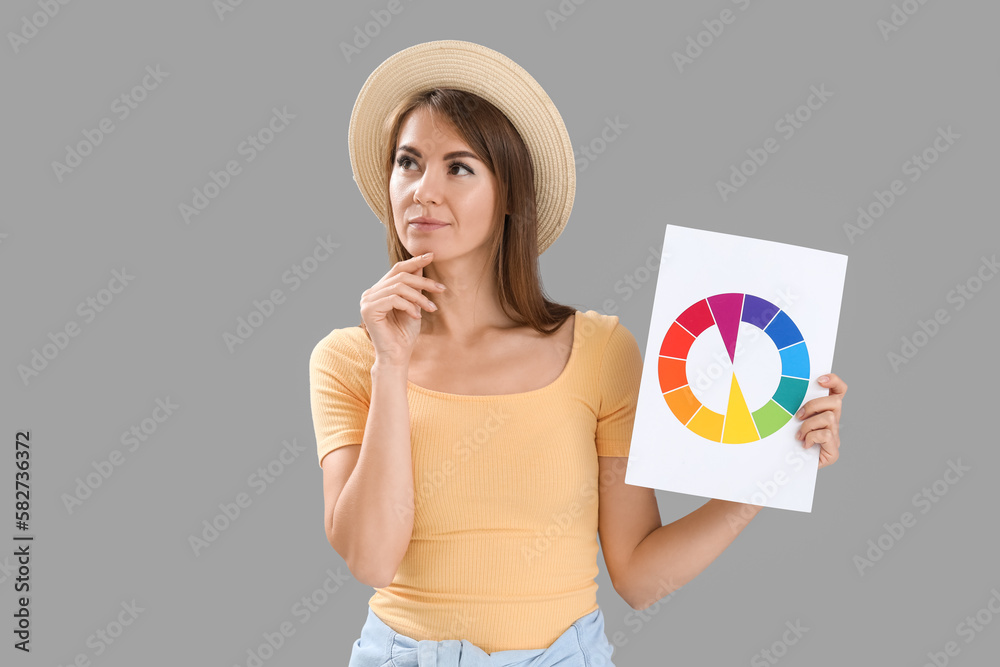 Thoughtful young woman with paint color palette on grey background