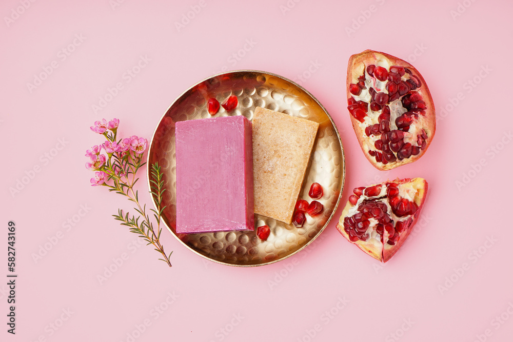 Plate with natural soap bars, flowers and pomegranate on pink background