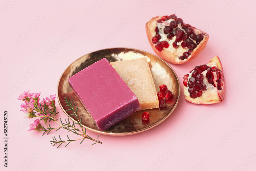 Plate with natural soap bars, flowers and pomegranate on pink background