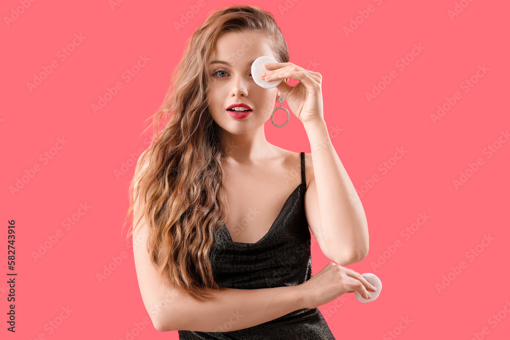 Young woman removing makeup with cotton pad on red background