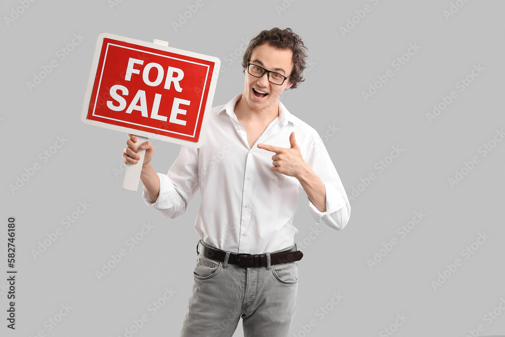 Real estate agent pointing at FOR SALE sign on grey background