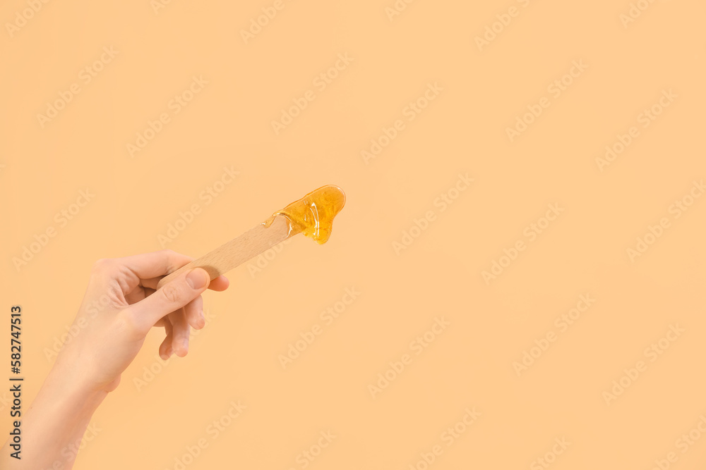 Female hand holding spatula with sugaring paste on beige background