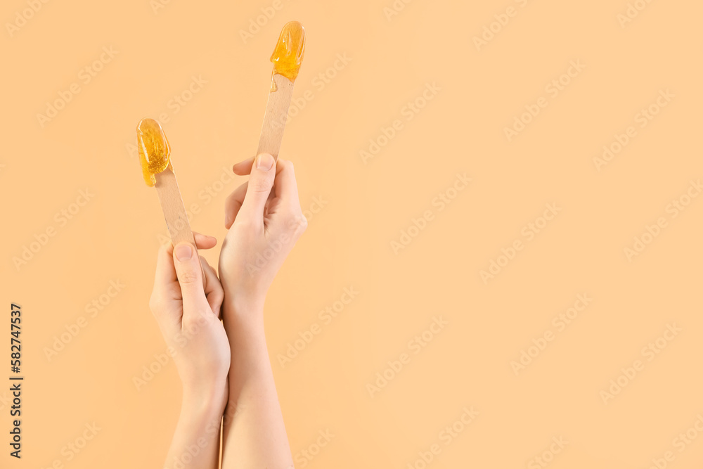 Female hands holding spatulas with sugaring paste on beige background