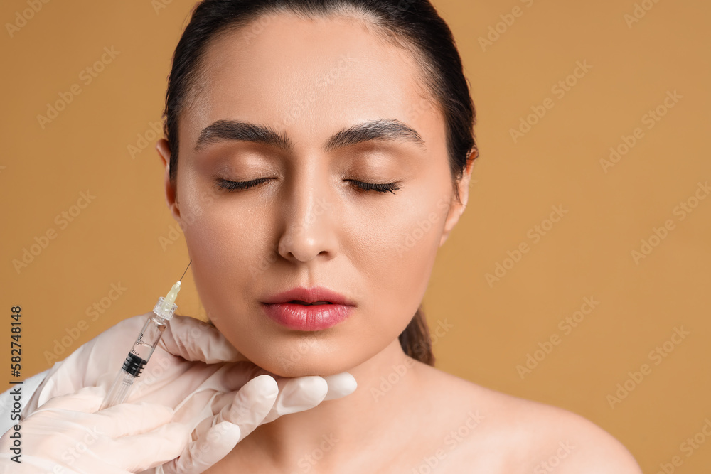 Young woman receiving filler injection in face against beige background