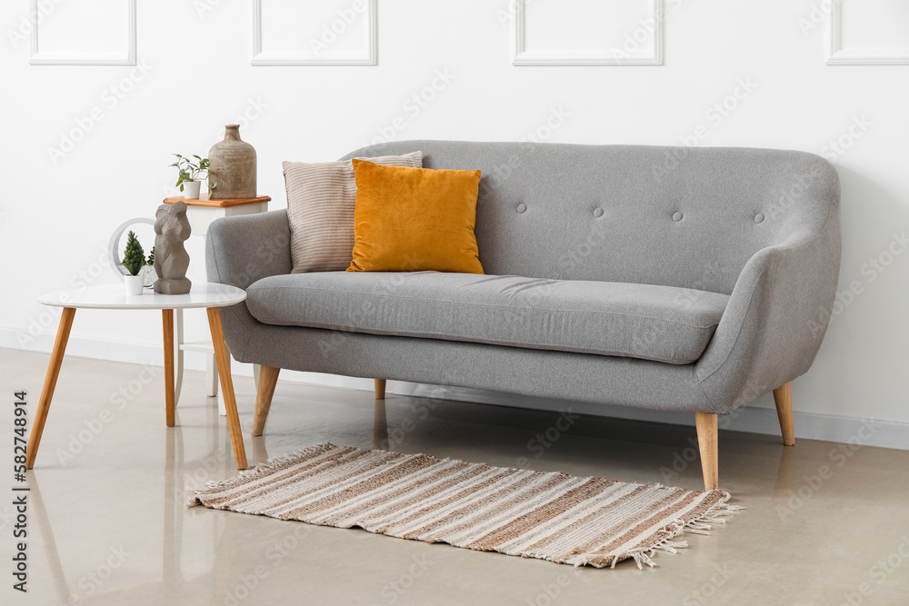 Cozy grey sofa with cushions and houseplants on tables near white wall