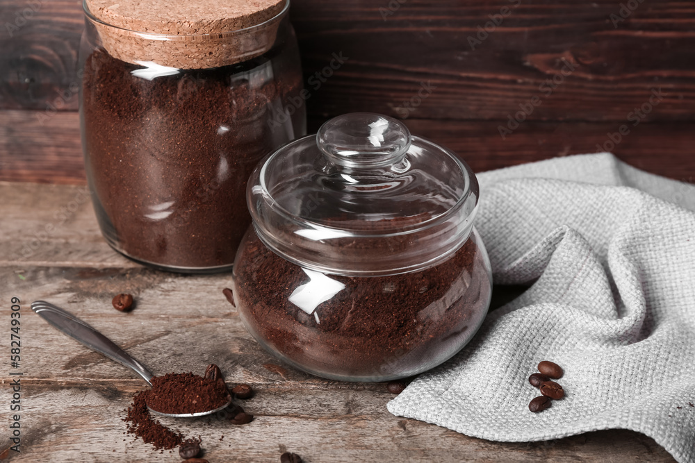 Jars and spoon of coffee powder with beans on wooden table, closeup