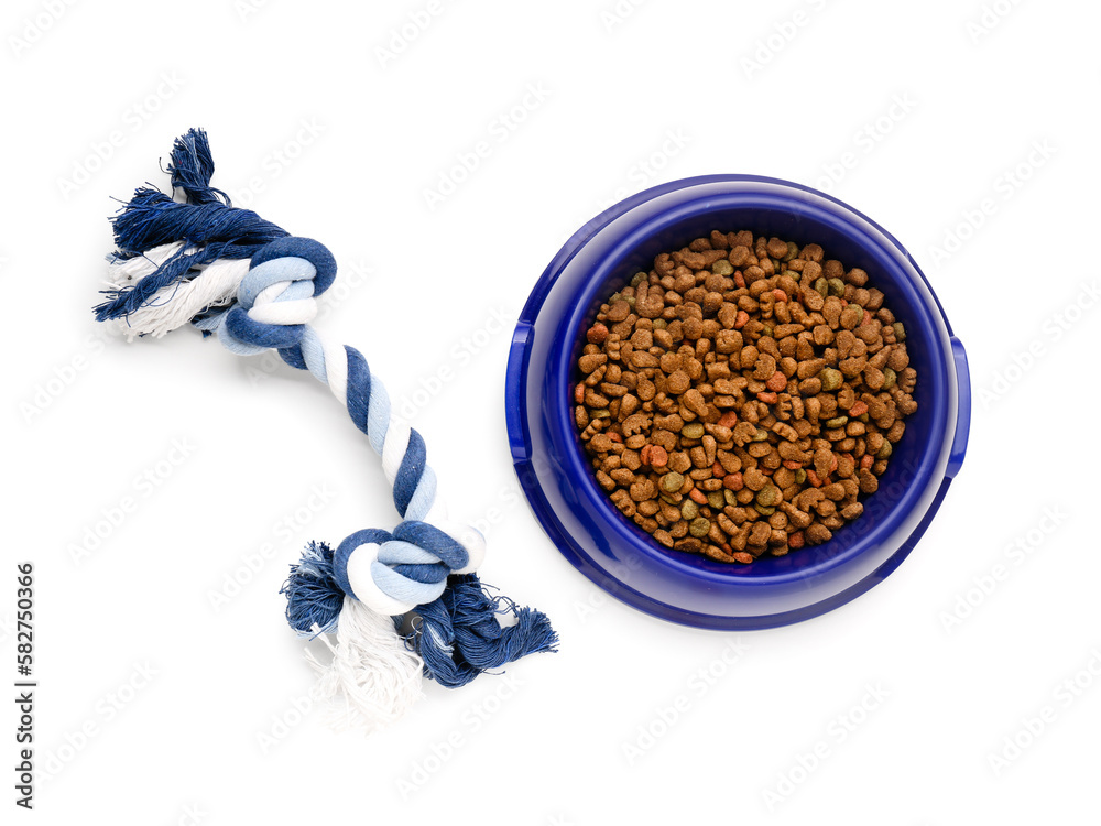 Bowl of dry pet food and cotton toy on white background