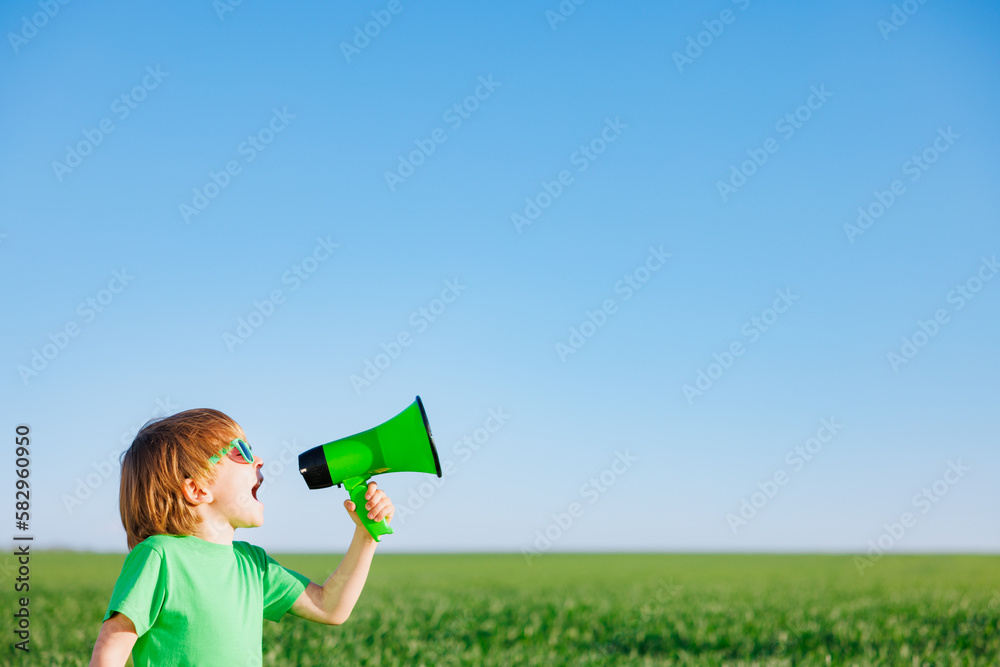 Happy child shouting through loudspeaker against blue summer sky