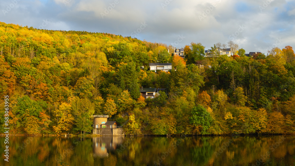 Beautiful german village with colorful foliage forest in the background and reflection in the Rursee