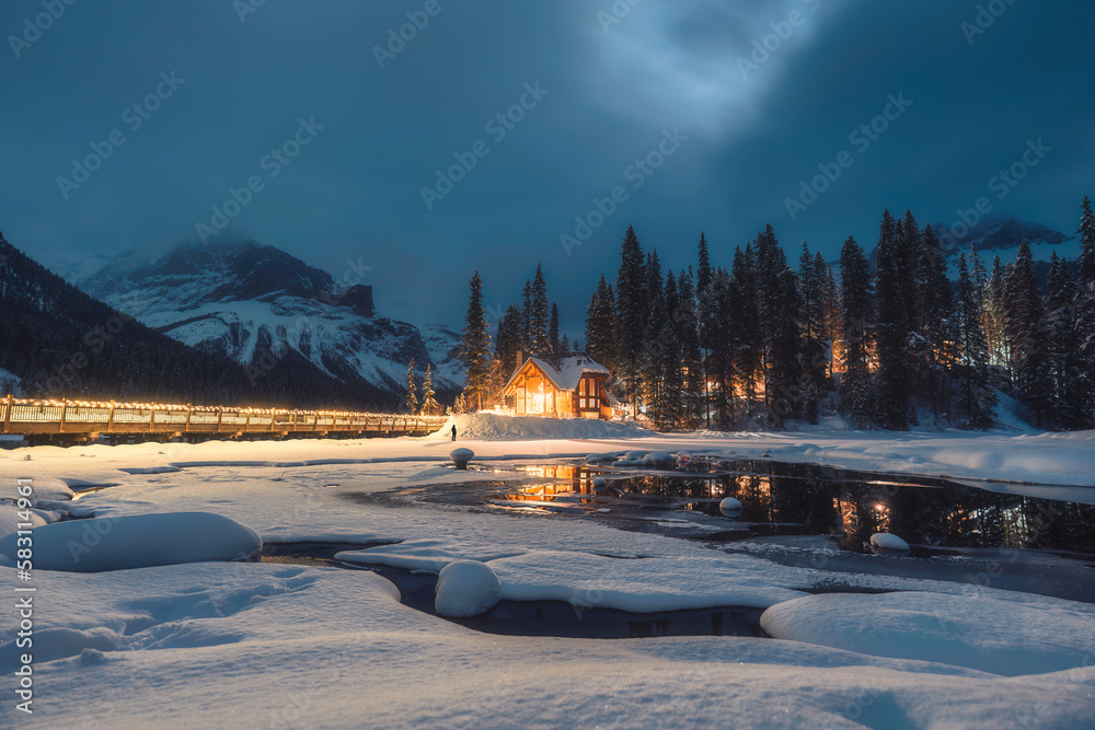 Frozen Emerald Lake with wooden lodge glowing in snowfall on winter at the night