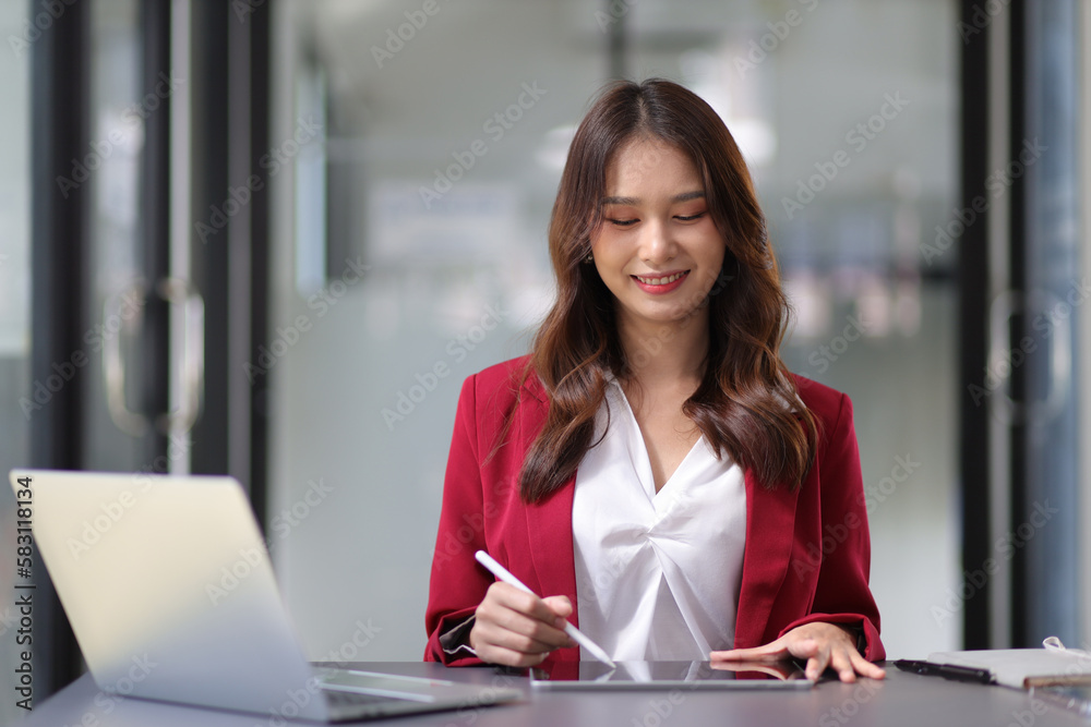 Young beautiful asian businesswoman in office working with laptop using tablet to work with electron