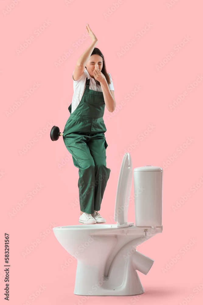 Funny female plumber with plunger and toilet bowl on pink background