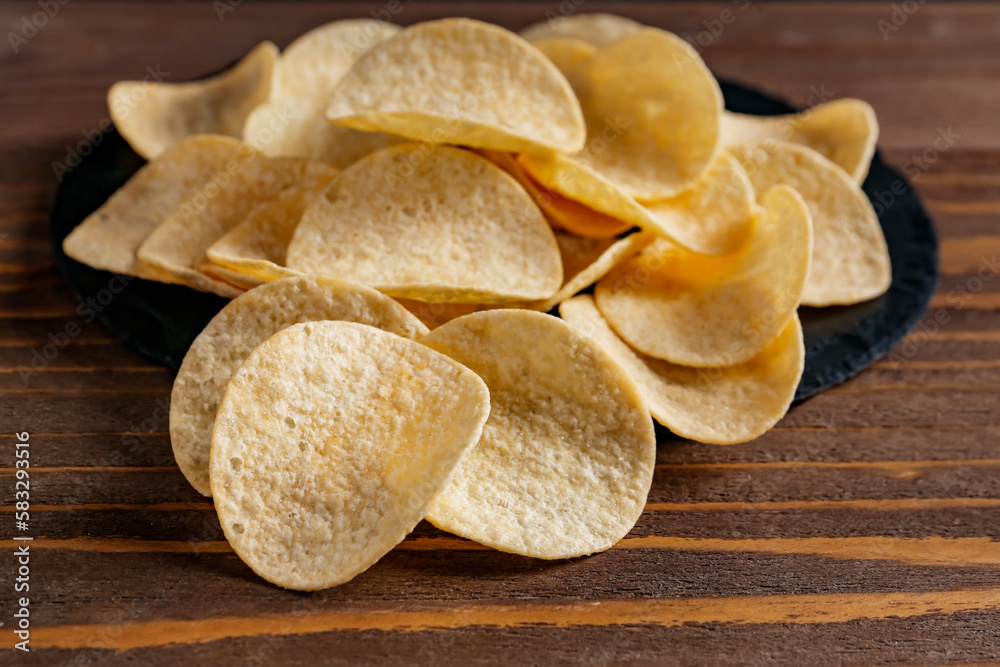 Heap of delicious potato chips on brown wooden table