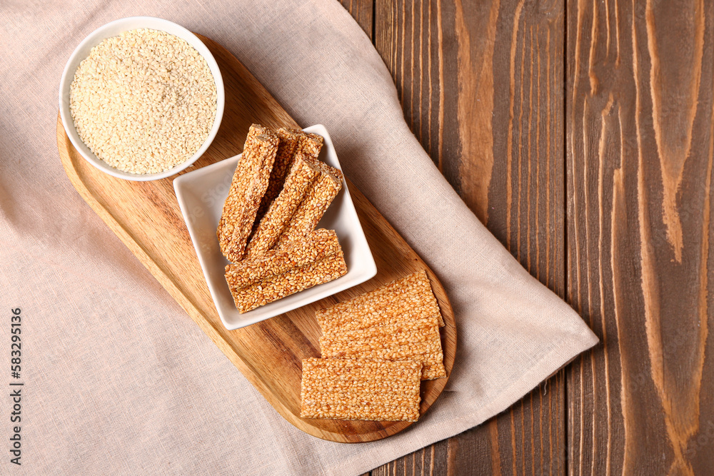 Board with sweet kozinaki and sesame seeds on wooden background