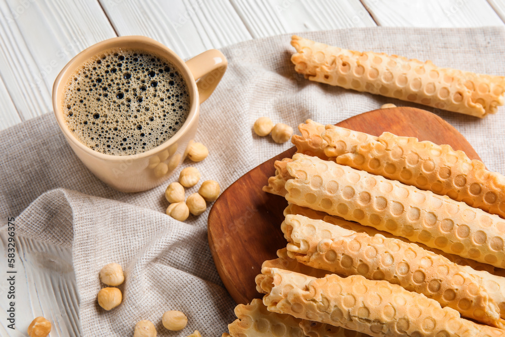 Board with delicious wafer rolls and cup of coffee on napkin, closeup