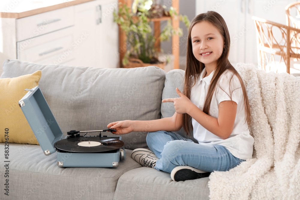 Little girl pointing at record player on sofa at home