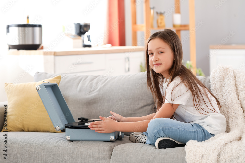 Little girl with vinyl disc and record player sitting on sofa at home