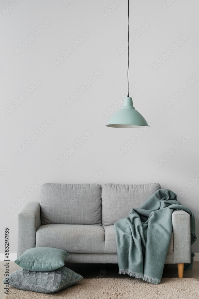 Cozy sofa with cushions and plaid near grey wall