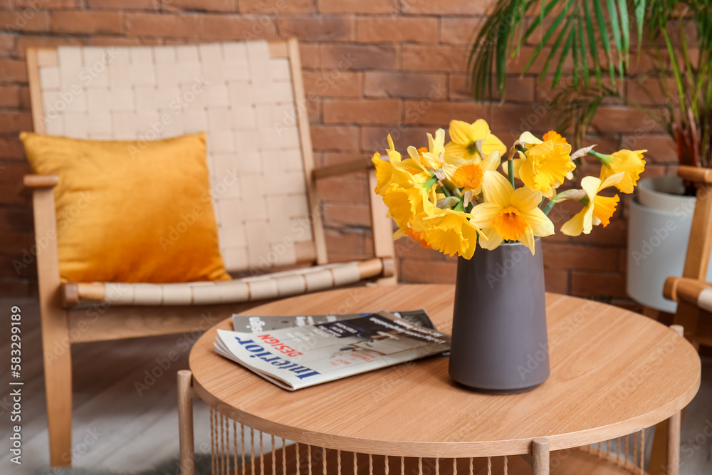 Vase with narcissus flowers and magazines on coffee table in living room