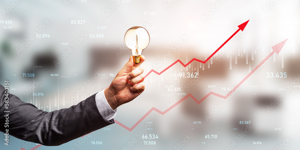 Close up of businessman hand holding light bulb with growing red business chart arrow on blurry offi