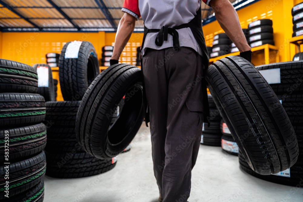 A male auto mechanic holding two tires in tire shop to change car wheels at service center or auto r