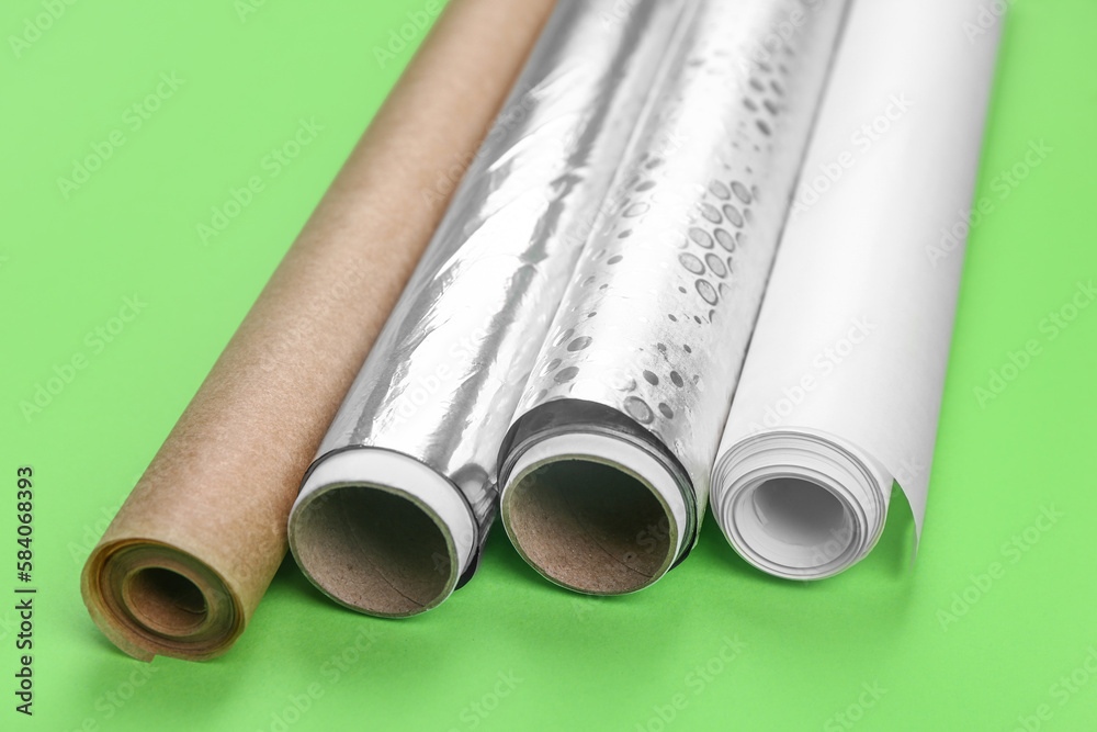 Rolls of aluminium foil and baking paper on green background, closeup