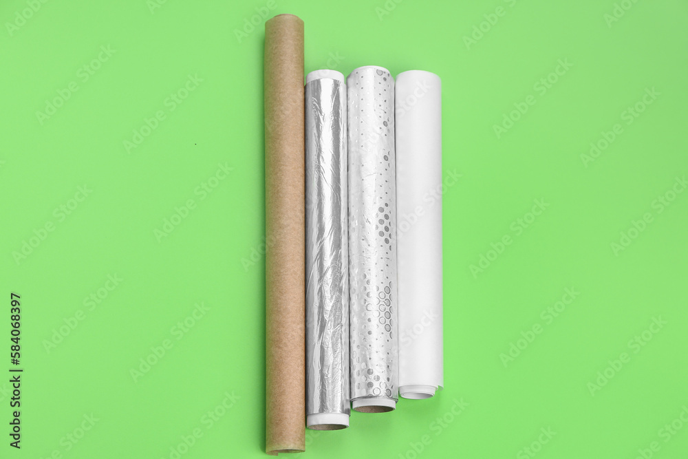 Rolls of aluminium foil and baking paper on green background