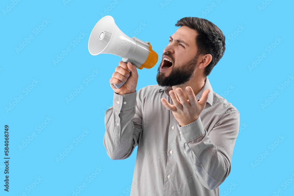 Angry young man shouting into megaphone on blue background